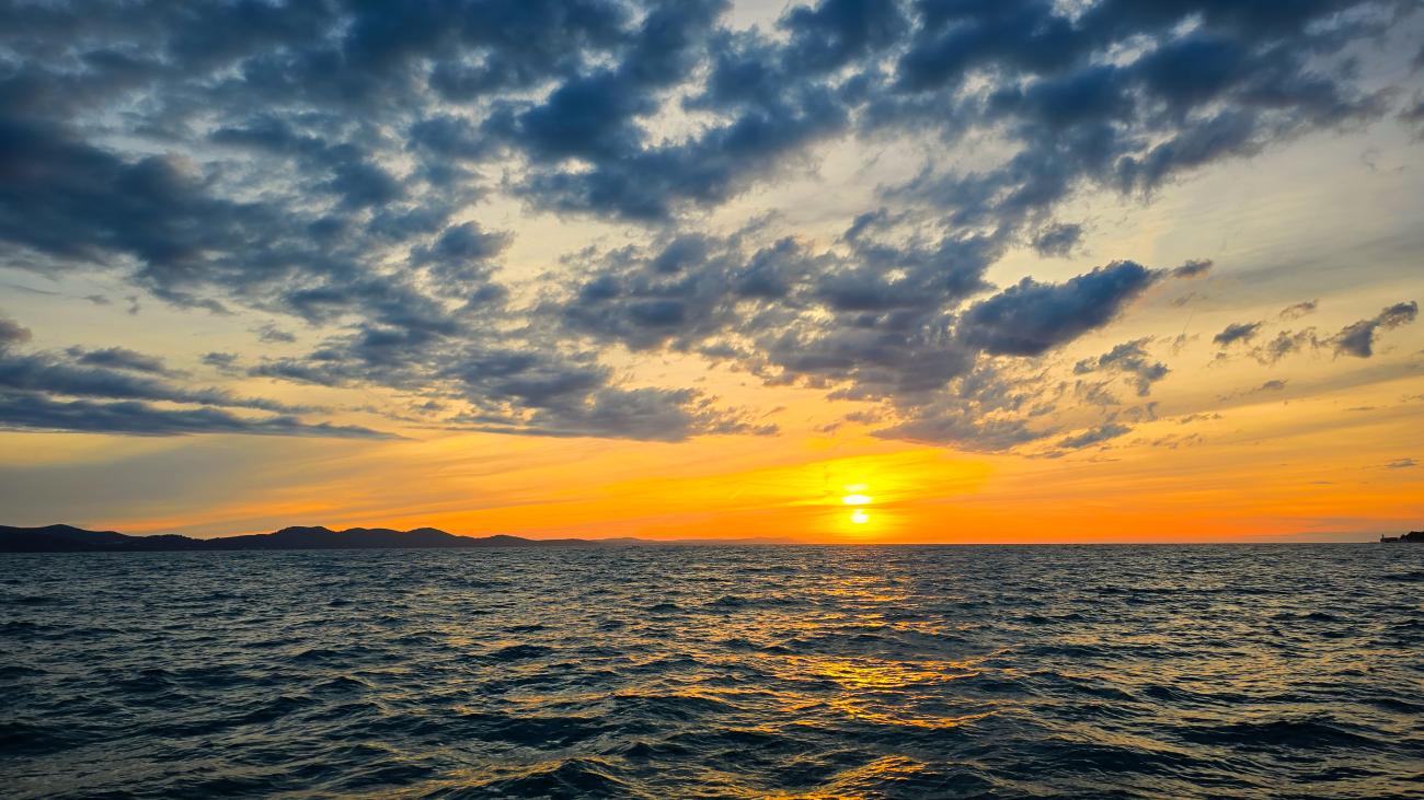 A golden sunset casting warm light over the Adriatic Sea along the Croatian coast.