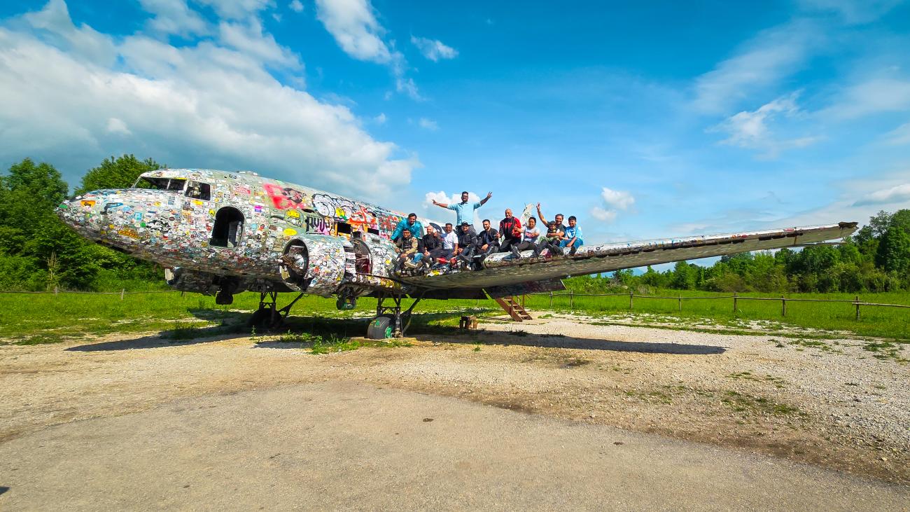 Tour group sitting on a sticker-covered abandoned airplane, a quirky roadside attraction in the Balkans.