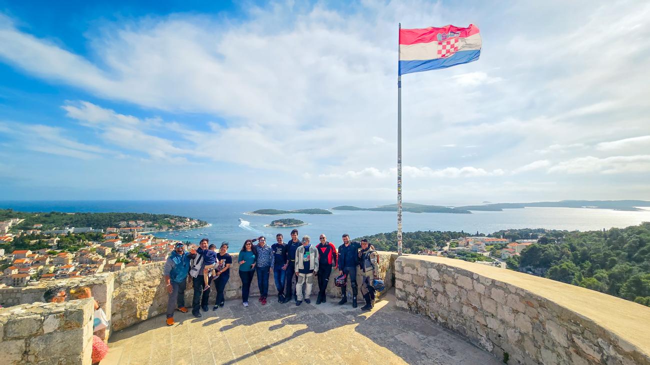 Tour group posing at the Hvar fortress in Croatia with the Croatian flag flying and Adriatic islands in the background.