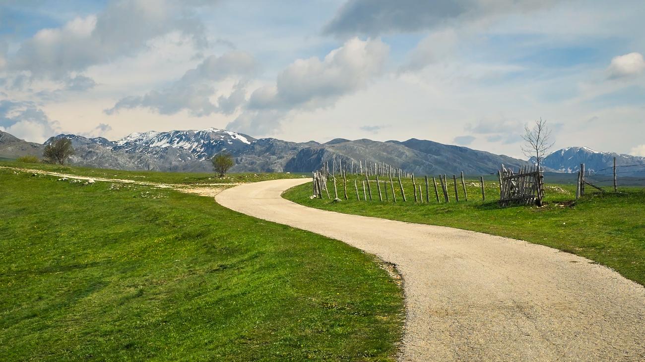 A winding country road leading toward snow-capped mountains in the Montenegrin highlands.
