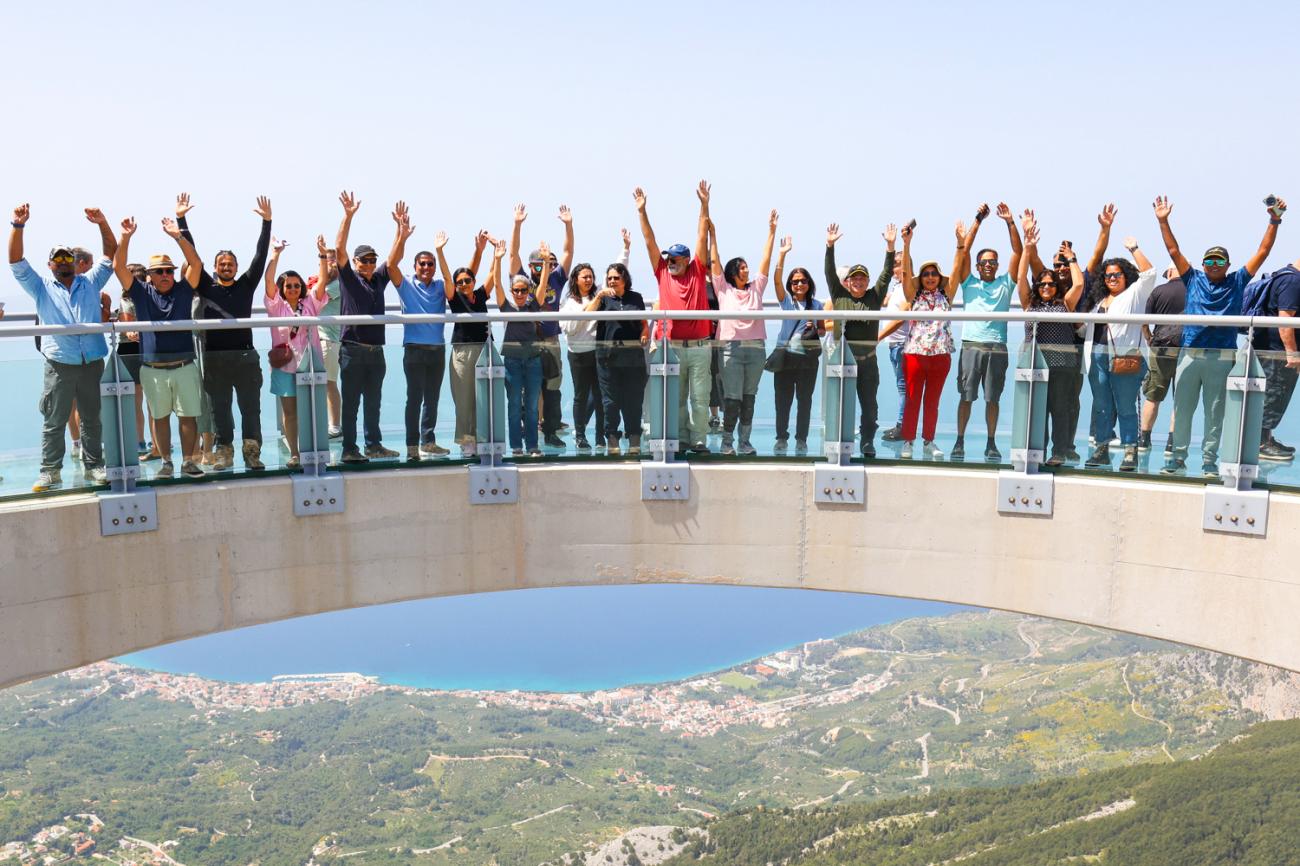 Tour group waving from a glass skywalk observation deck high above the Balkan coastline