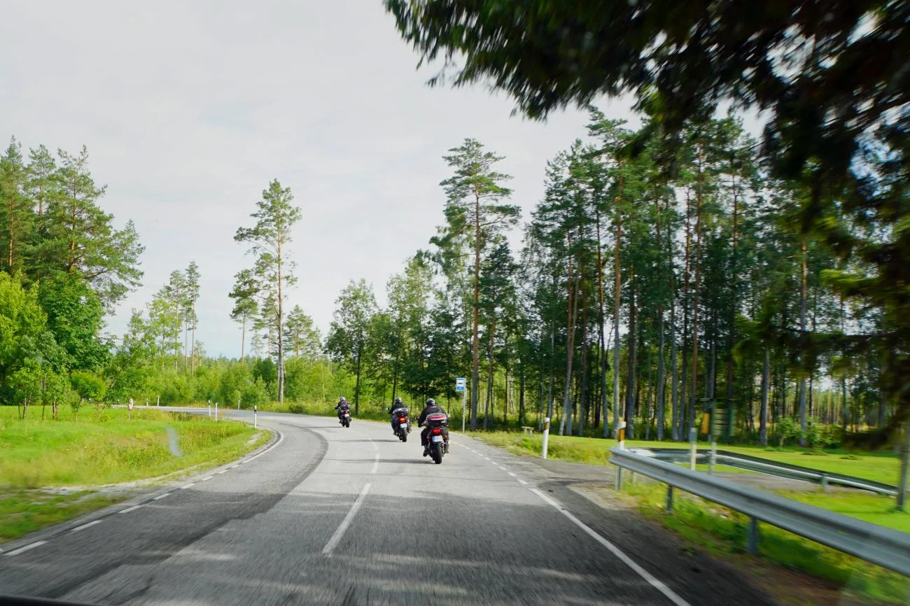 Motorcycles riding a tree-lined road on the Northern Europe tour