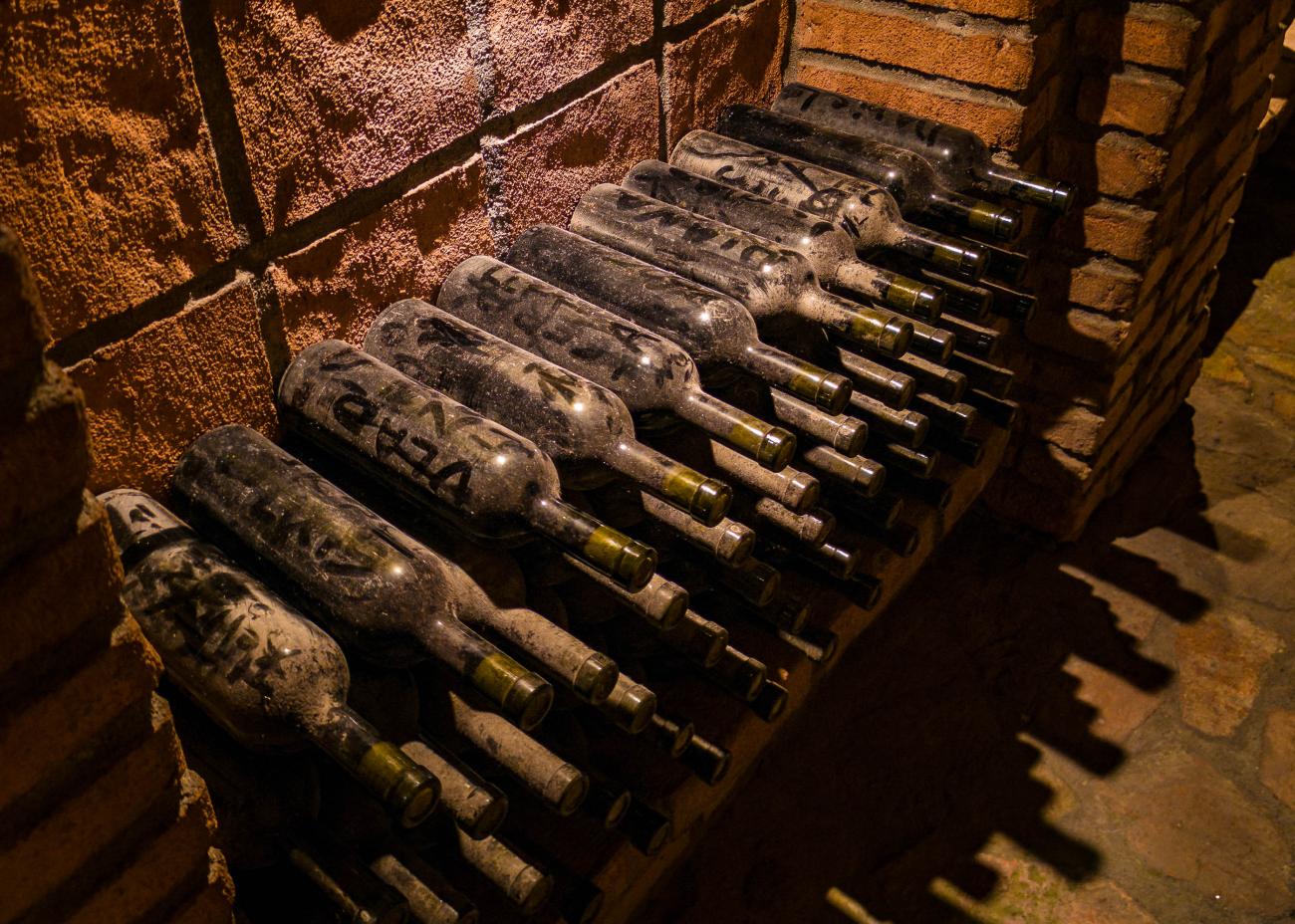 Dust-covered wine bottles aging on brick racks in a traditional Georgian wine cellar.