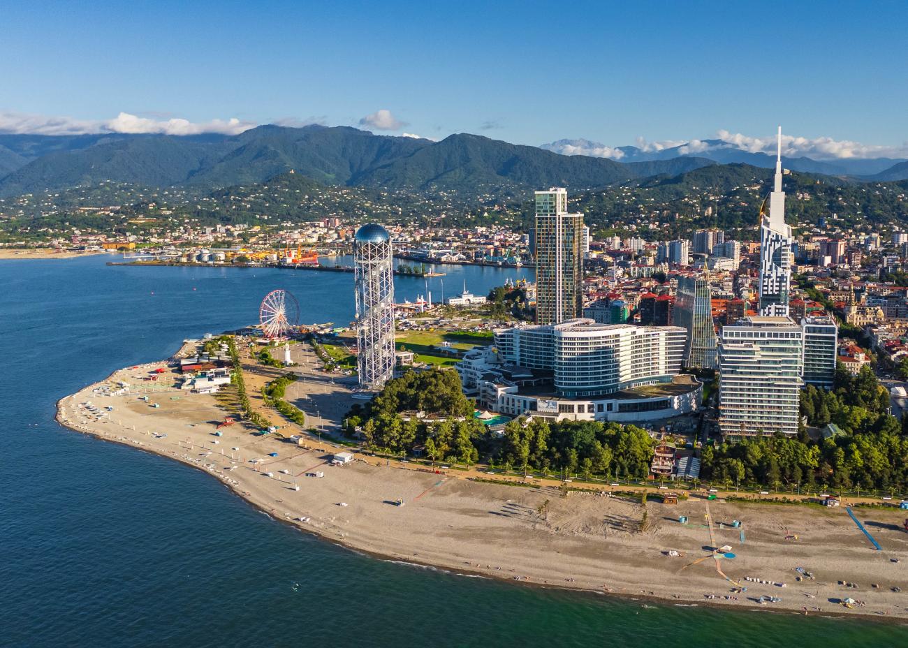 Aerial view of Batumi on the Black Sea coast with modern skyline and Caucasus mountains in the background.