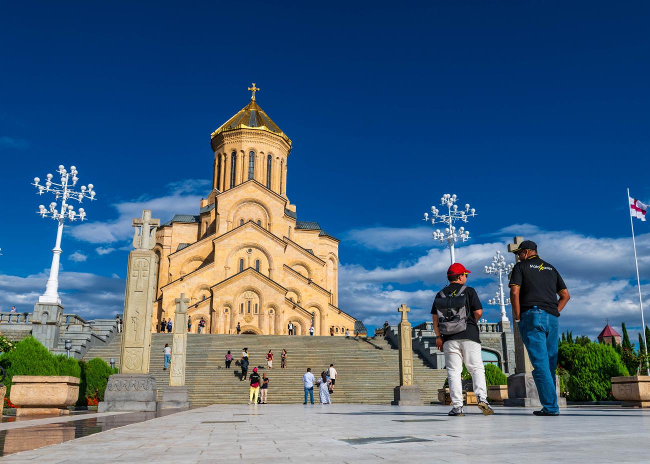 MotoRover tour riders visiting the Holy Trinity Cathedral of Tbilisi under a bright blue sky.