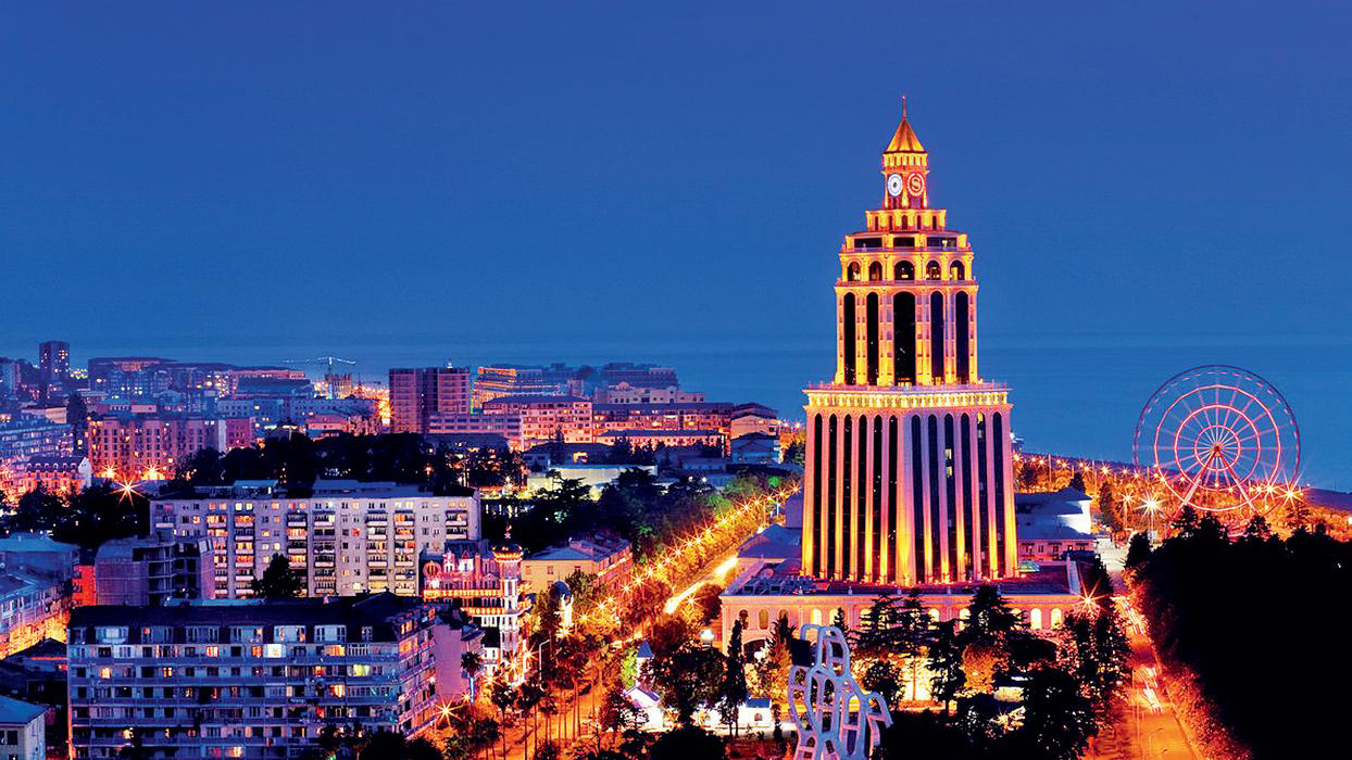 The illuminated Batumi clock tower and Ferris wheel glowing against a deep blue evening sky in the Georgian coastal city