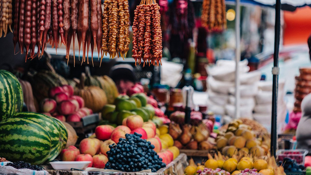 A vibrant Georgian market stall displaying hanging churchkhela walnut candy strings alongside colorful fresh fruits and watermelons