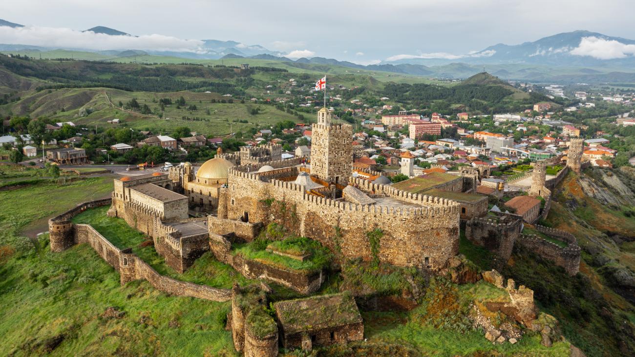 Aerial view of the restored Rabati Castle complex in Akhaltsikhe with its stone towers and gold-domed mosque against green Caucasus foothills