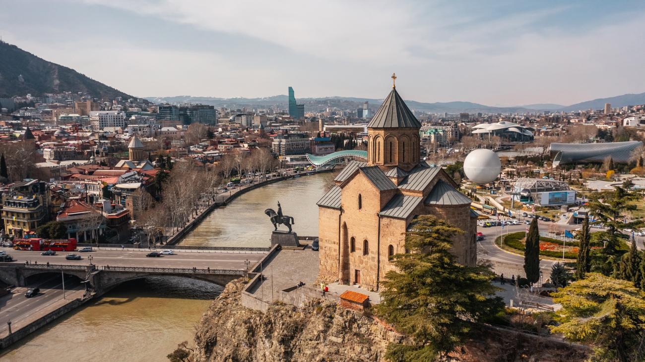 Aerial view of Tbilisi showing Sioni Cathedral on a rocky outcrop, Metekhi Bridge with an equestrian statue, and the Kura River