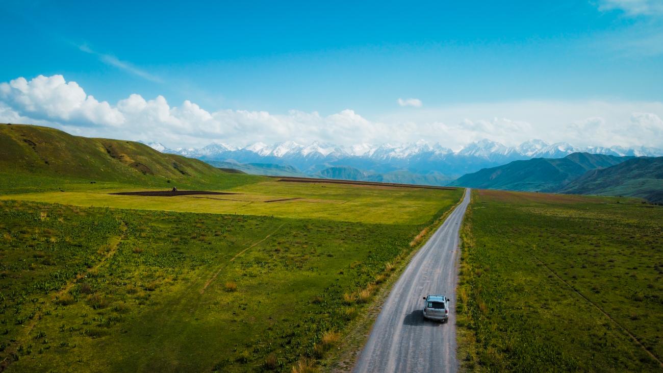 Aerial view of SUV on lone road towards snow-capped mountains