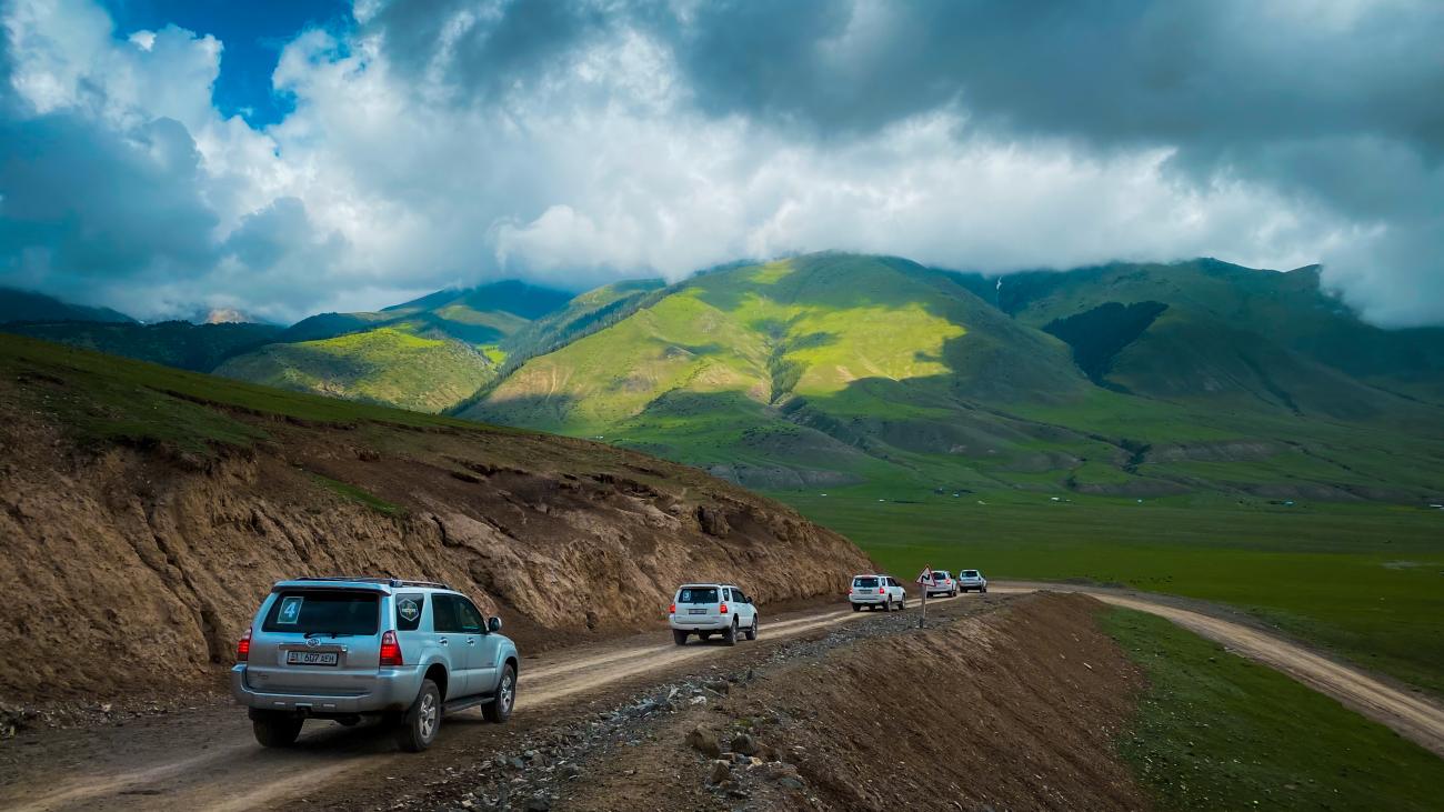 SUV convoy on dirt road through green mountains Kyrgyzstan