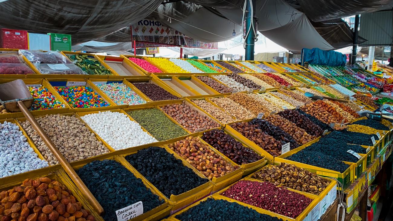 Rows of colorful dried fruits, nuts, and sweets displayed at a traditional Kyrgyz bazaar market stall.