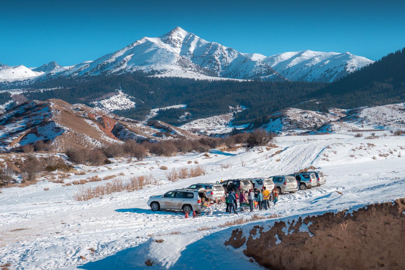 Tour vehicles and travelers taking a pit stop on a snowy plateau with towering mountain peaks in the background