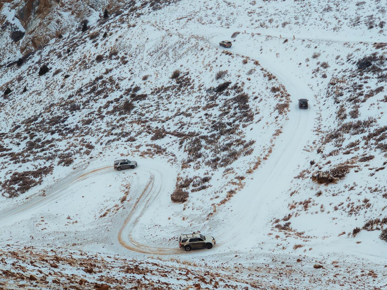 4x4 vehicles zigzagging up a steep snowy mountain pass in Kyrgyzstan