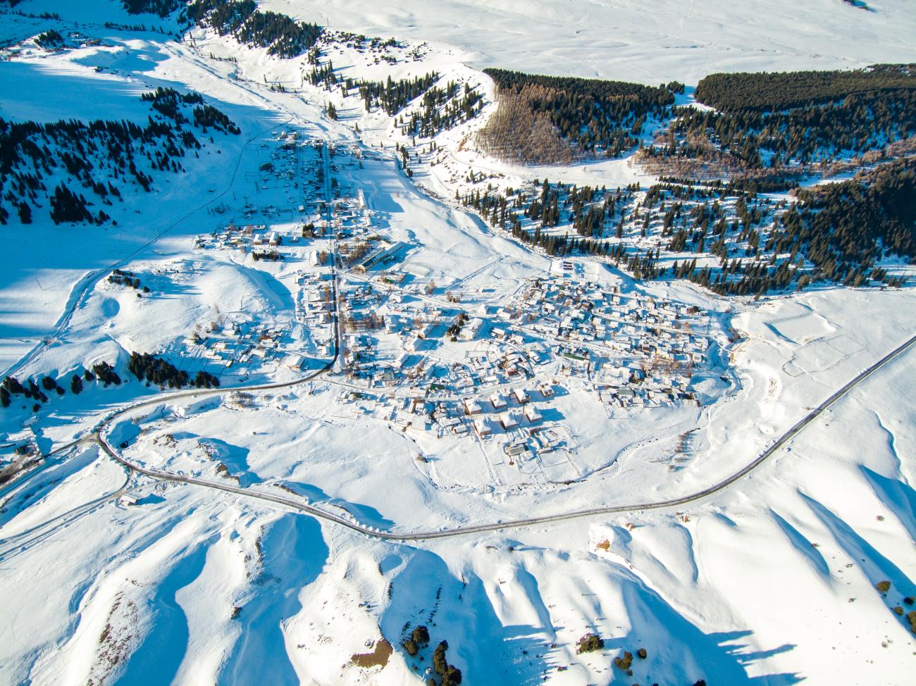 Aerial view of a snow-covered mountain village nestled among forested slopes in Kyrgyzstan