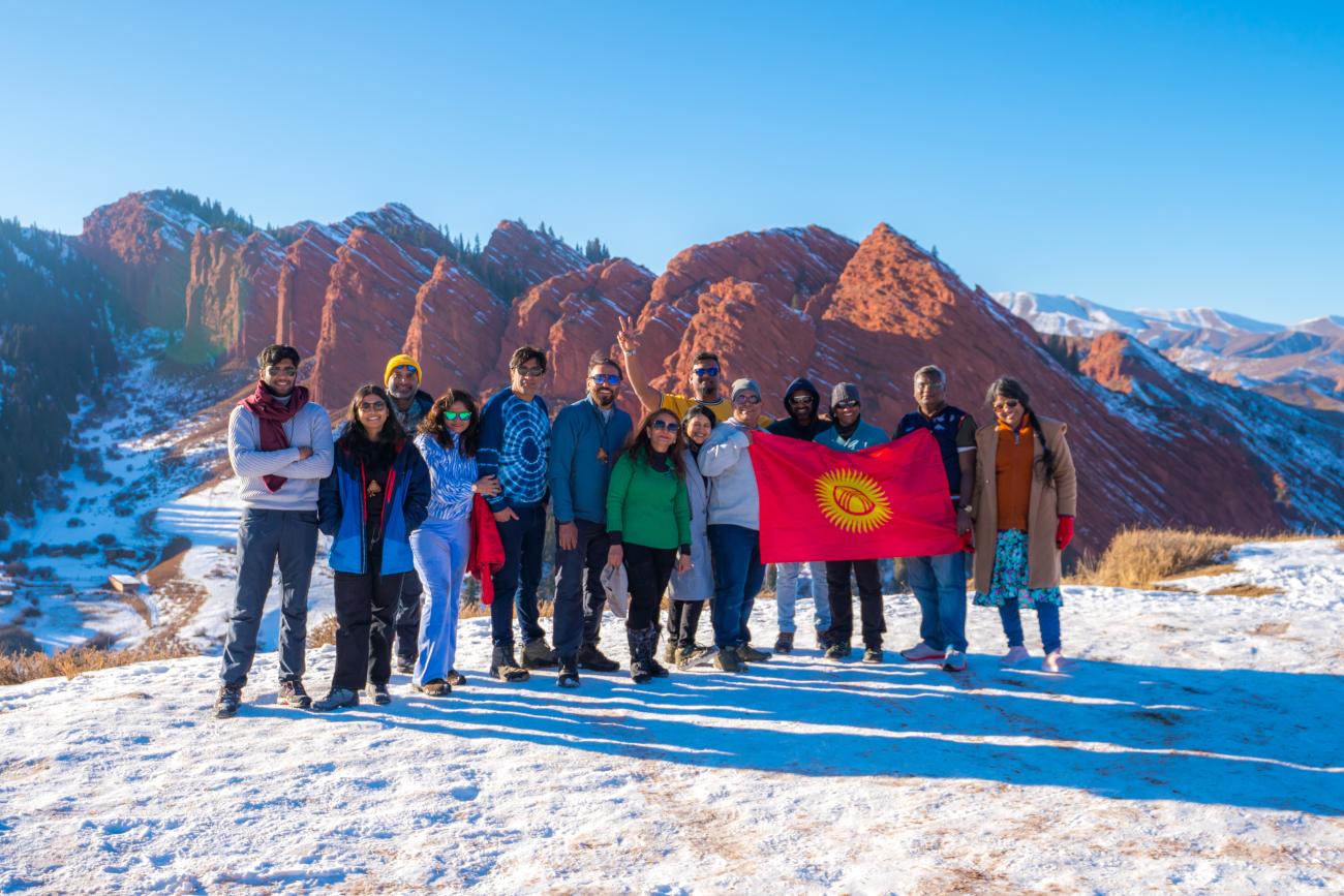 A tour group holding the Kyrgyz flag in front of the red rock formations of Jeti-Oguz in winter