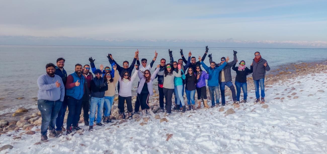 A large tour group cheering with arms raised on the snowy shore of Issyk-Kul lake
