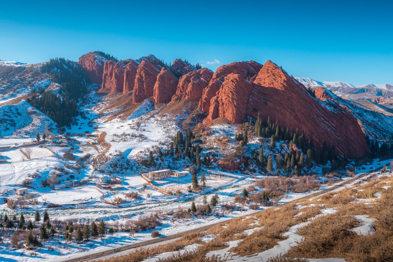 The striking red sandstone formations of Jeti-Oguz covered in snow under a bright blue sky