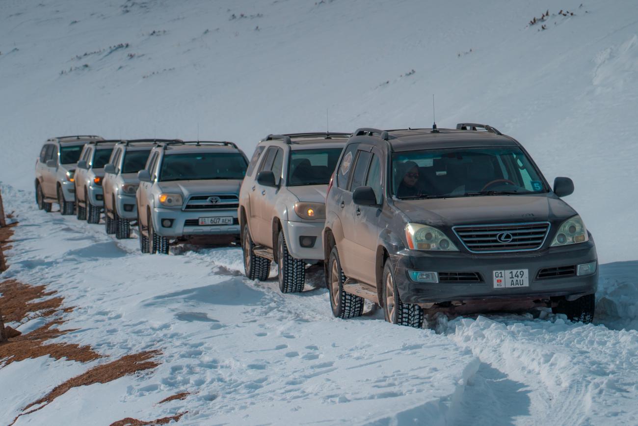 A convoy of 4x4 SUVs lined up on a narrow snowy mountain road in Kyrgyzstan