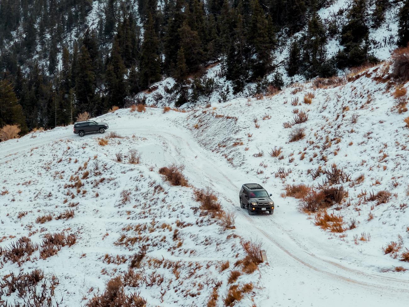Two SUVs navigating a tight hairpin turn on a snowy forest trail in the Kyrgyz mountains