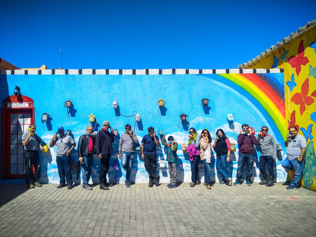 Tour group posing by a vibrant blue mural wall with vintage telephones in a Moroccan town.