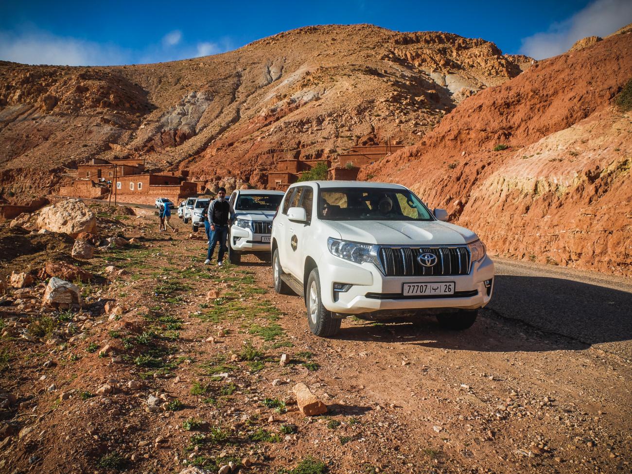 Toyota Land Cruisers driving through the red clay hills of the Dades Valley in Morocco.