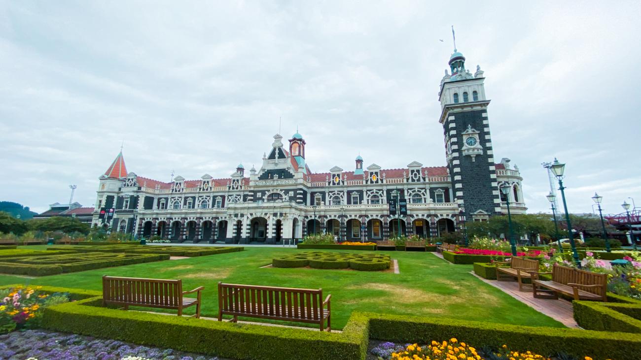 Ornate Dunedin Railway Station with its Flemish Renaissance architecture and manicured gardens in the foreground.