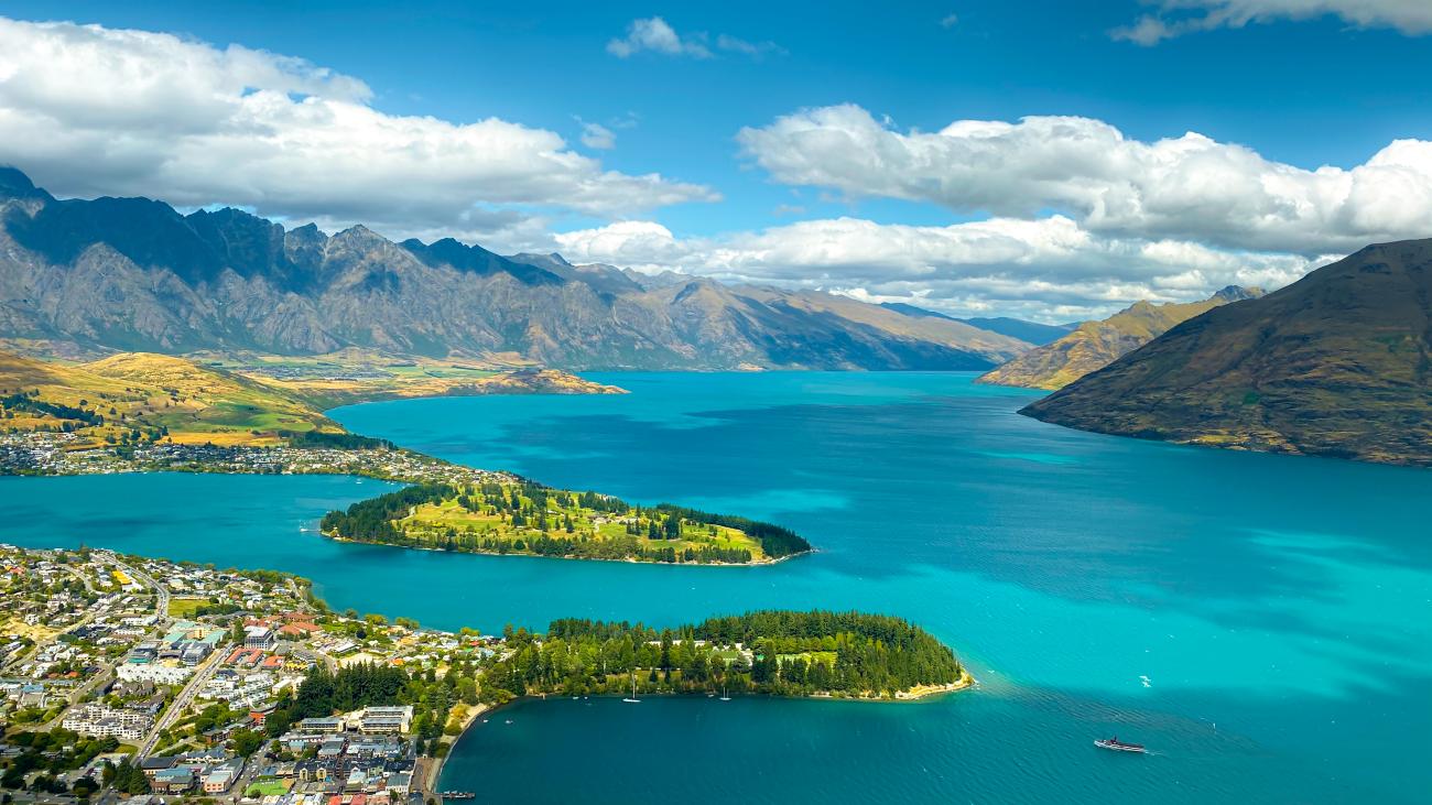 Aerial view of Queenstown nestled along turquoise Lake Wakatipu with the Remarkables mountain range in the background.