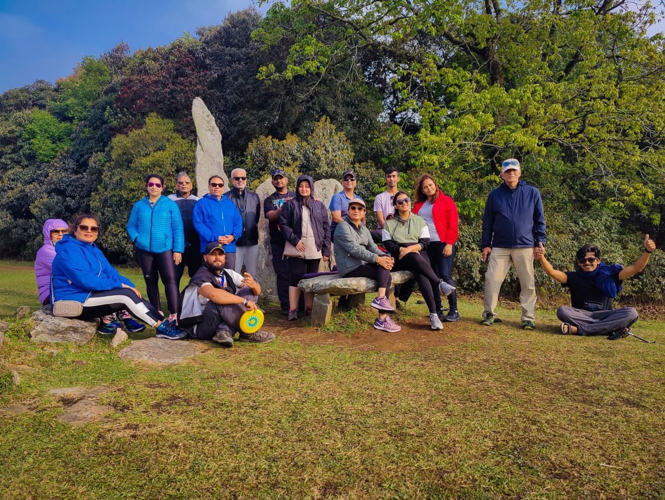 A group of travelers posing near a stone monolith surrounded by lush green trees in Meghalaya.