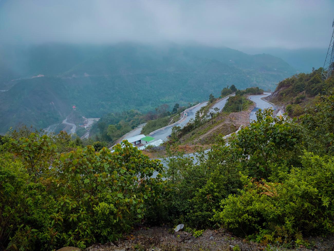 A winding mountain road cutting through misty green hills in Northeast India.