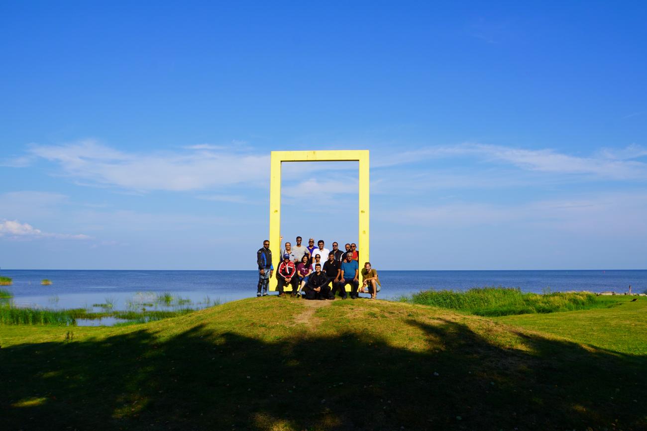 Tour group posing inside a large yellow frame sculpture overlooking the Baltic Sea in Estonia.