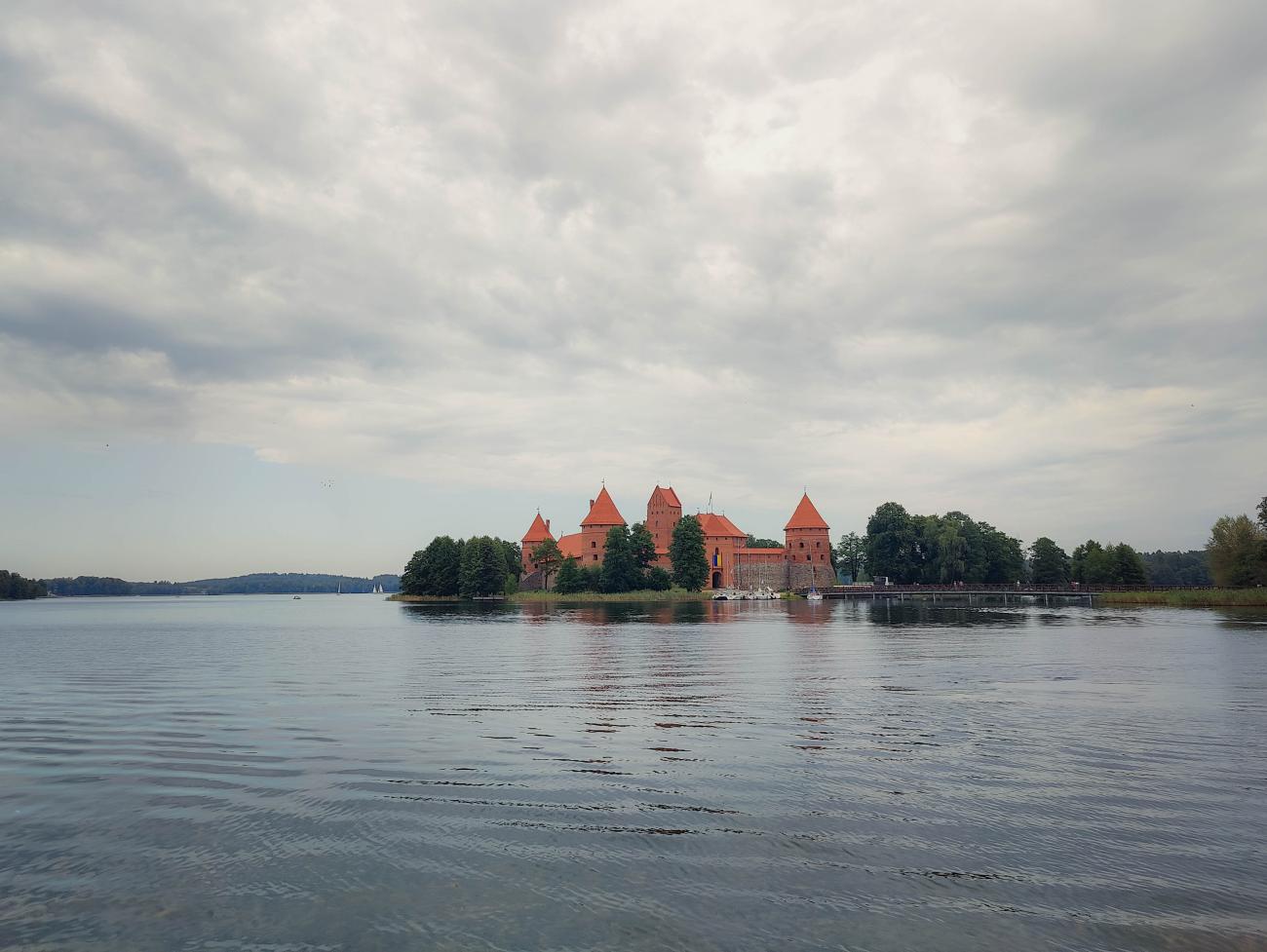 Trakai Island Castle reflected in the lake under dramatic overcast skies in Lithuania.