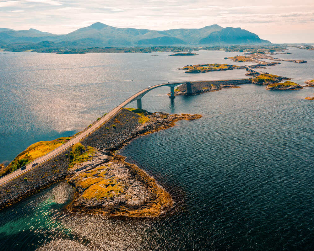 Aerial view of the Atlantic Road bridge curving over the sea between rocky islands at sunset in Norway.