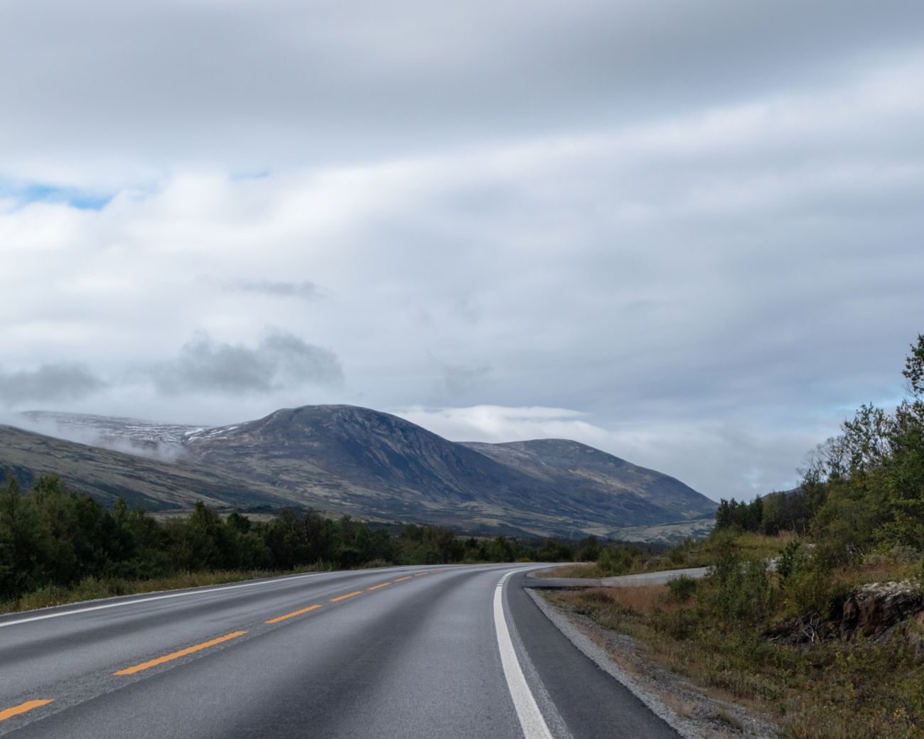 Curving road through the Norwegian highlands under an overcast sky with mountains in the distance.