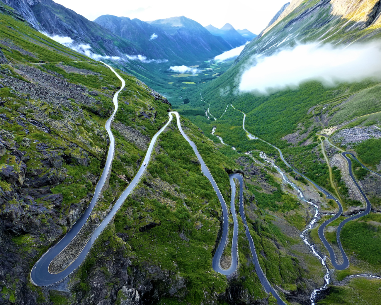Dramatic aerial view of Trollstigen's steep hairpin switchbacks descending into a green valley with waterfalls.