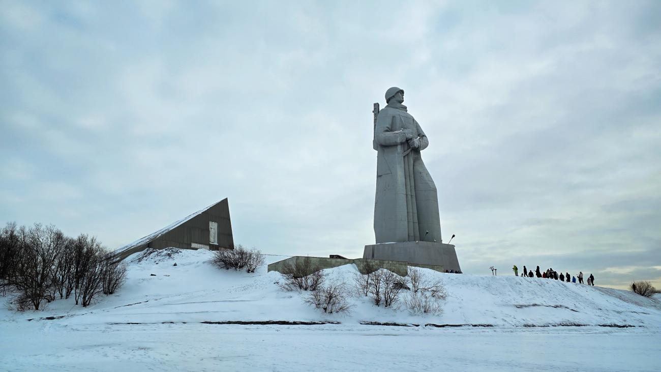 The towering Alyosha war memorial statue standing on a snow-covered hill in Murmansk with visitors walking nearby.