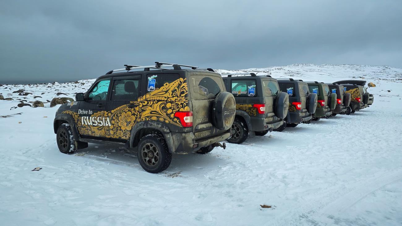 A convoy of MotoRover-branded UAZ Patriot SUVs with golden livery lined up on a snowy Russian plateau.