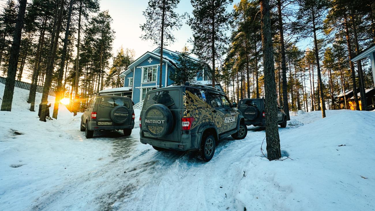 MotoRover SUVs parked outside a blue wooden cabin in a snowy pine forest with golden sunlight filtering through the trees.