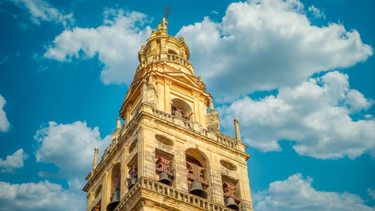 Close-up of the Mezquita-Cathedral bell tower in Cordoba bathed in golden sunlight against a blue sky.