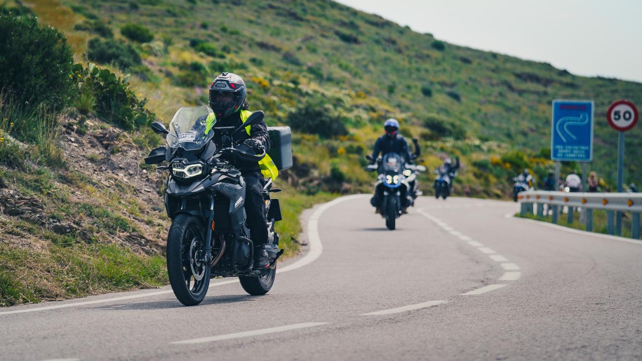 Three adventure motorcyclists riding in formation along a winding mountain road through green Spanish hillsides.