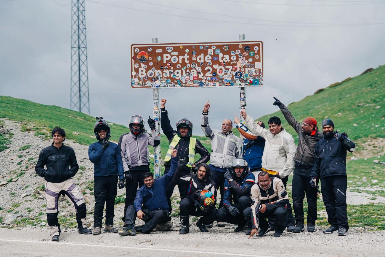 Group of motorcycle tour riders celebrating at the Port de la Bonaigua mountain pass sign at 2072 metres in the Spanish Pyrenees.