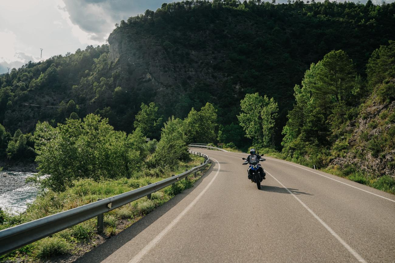 Solo motorcyclist riding through a forested river gorge on a mountain road in northern Spain.