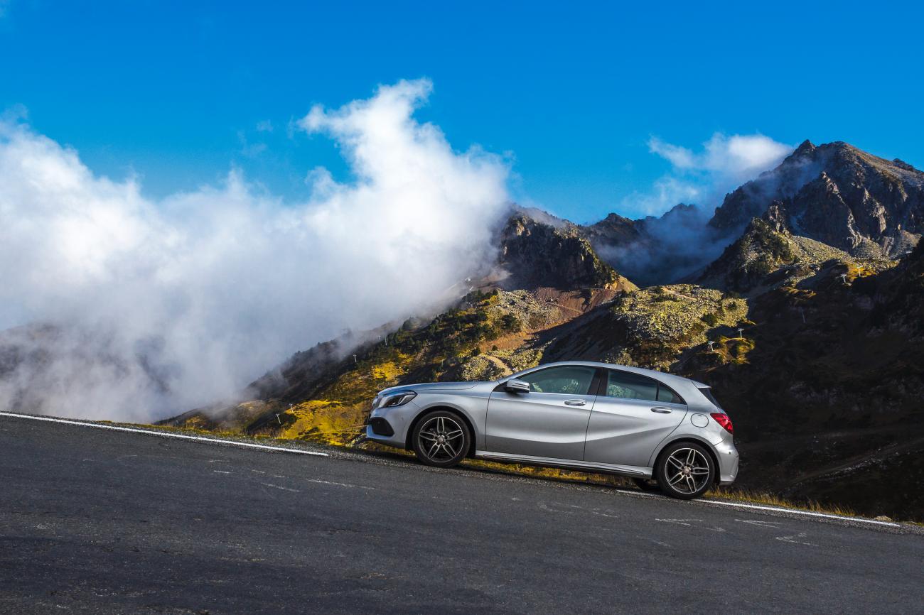 Silver Mercedes-Benz A-Class on a high-altitude Pyrenees road with dramatic clouds rolling over rugged mountain peaks.