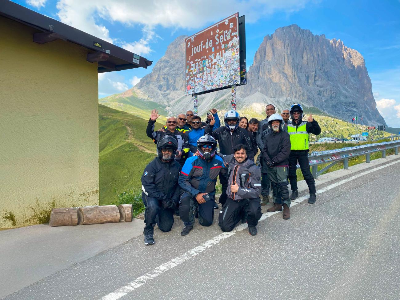 Motorcycle tour group posing for a photo at Passo Sella with the Sassolungo peak in the Dolomites behind them.
